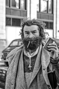 Street photography portrait of a man called Simion. A black scraggly beard, with a long necklace.