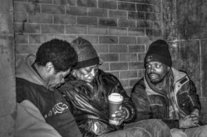 Three homeless people sit on Lower Wacker drive, in the cold Chicago winter, sharing a cup of coffee.